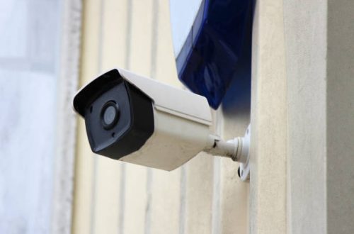 A security camera and burglar alarm in shot on a building wall.