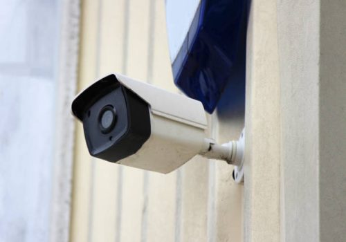 A security camera and burglar alarm in shot on a building wall.